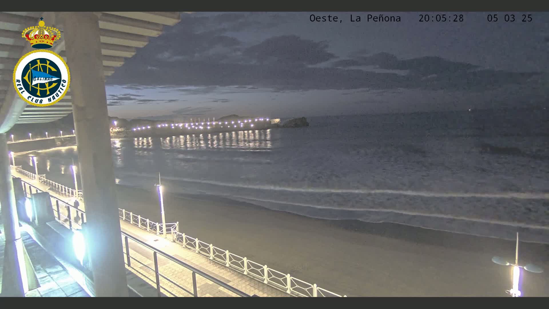 A nighttime view of a beach with a pier and calm waves under a cloudy sky.