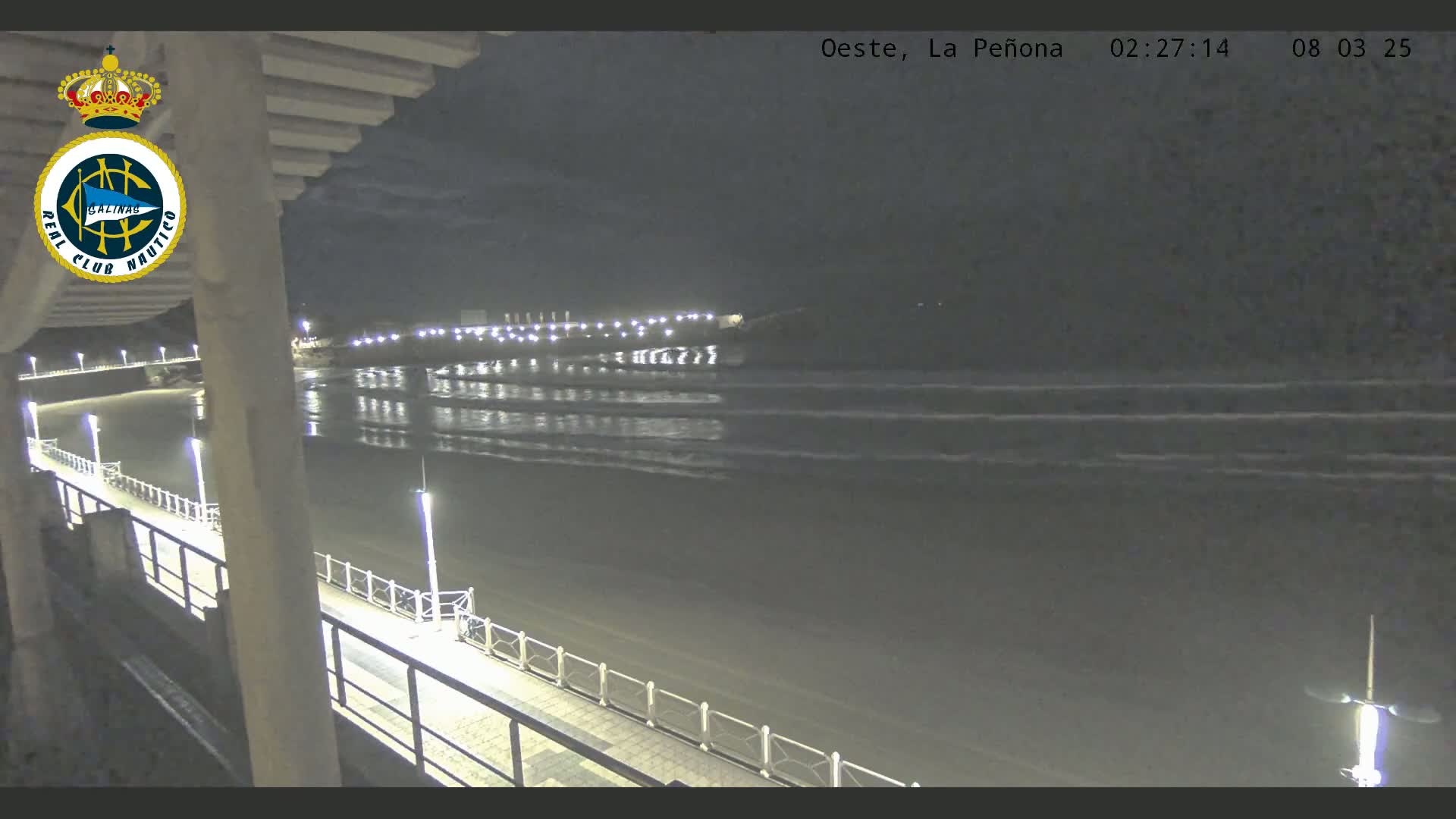 A nighttime view of a beach with calm waves, a boardwalk with lights, and a structure in the background.