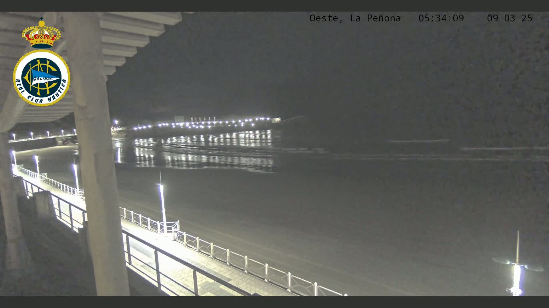 A nighttime view from a pier overlooking a calm, dark ocean reflecting lights from the shore.