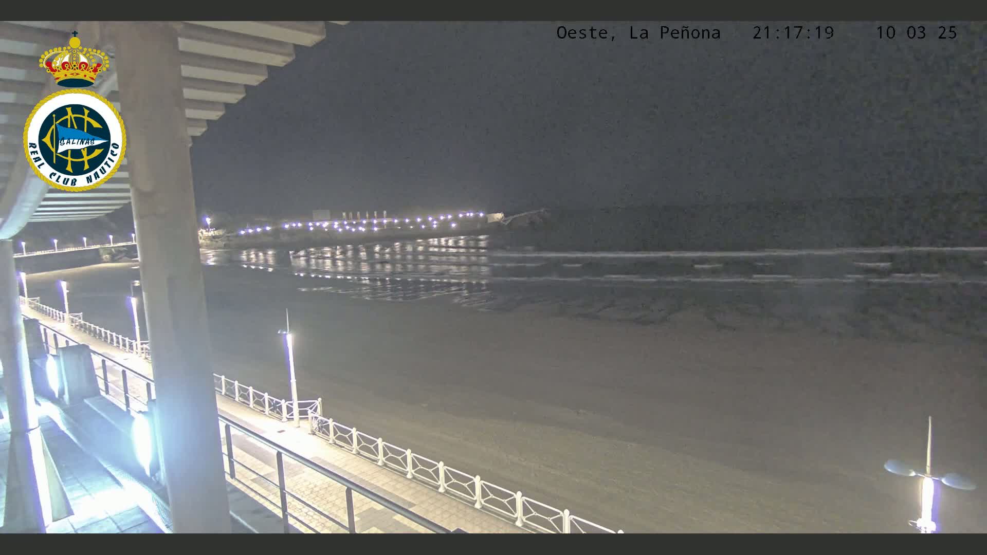 A nighttime view of a beach with calm waves under a dark sky, seen from an elevated vantage point along a lit walkway.