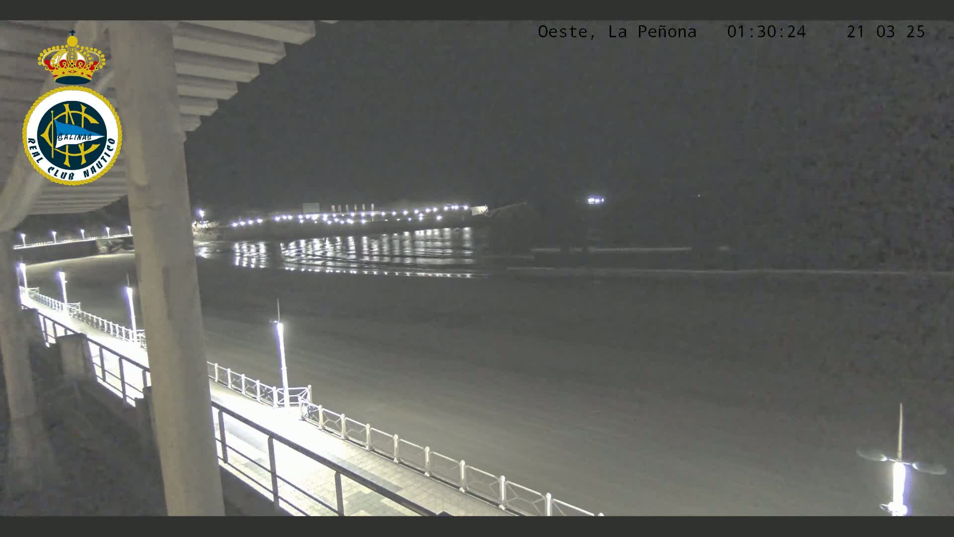 A nighttime view from a balcony overlooking a calm, dark body of water with a lit walkway along the shore.