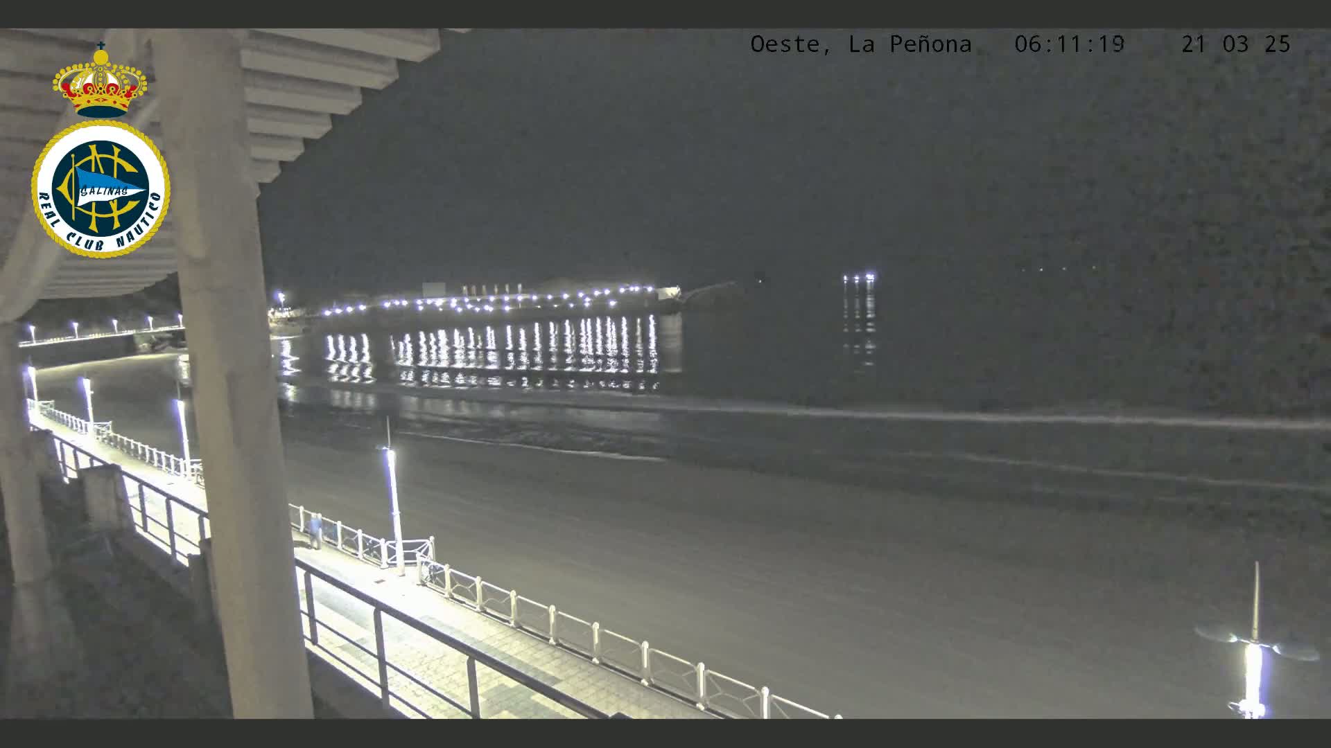 A nighttime view of a calm ocean with a brightly lit pier and boardwalk extending from the right side of the image, seen from a high vantage point.