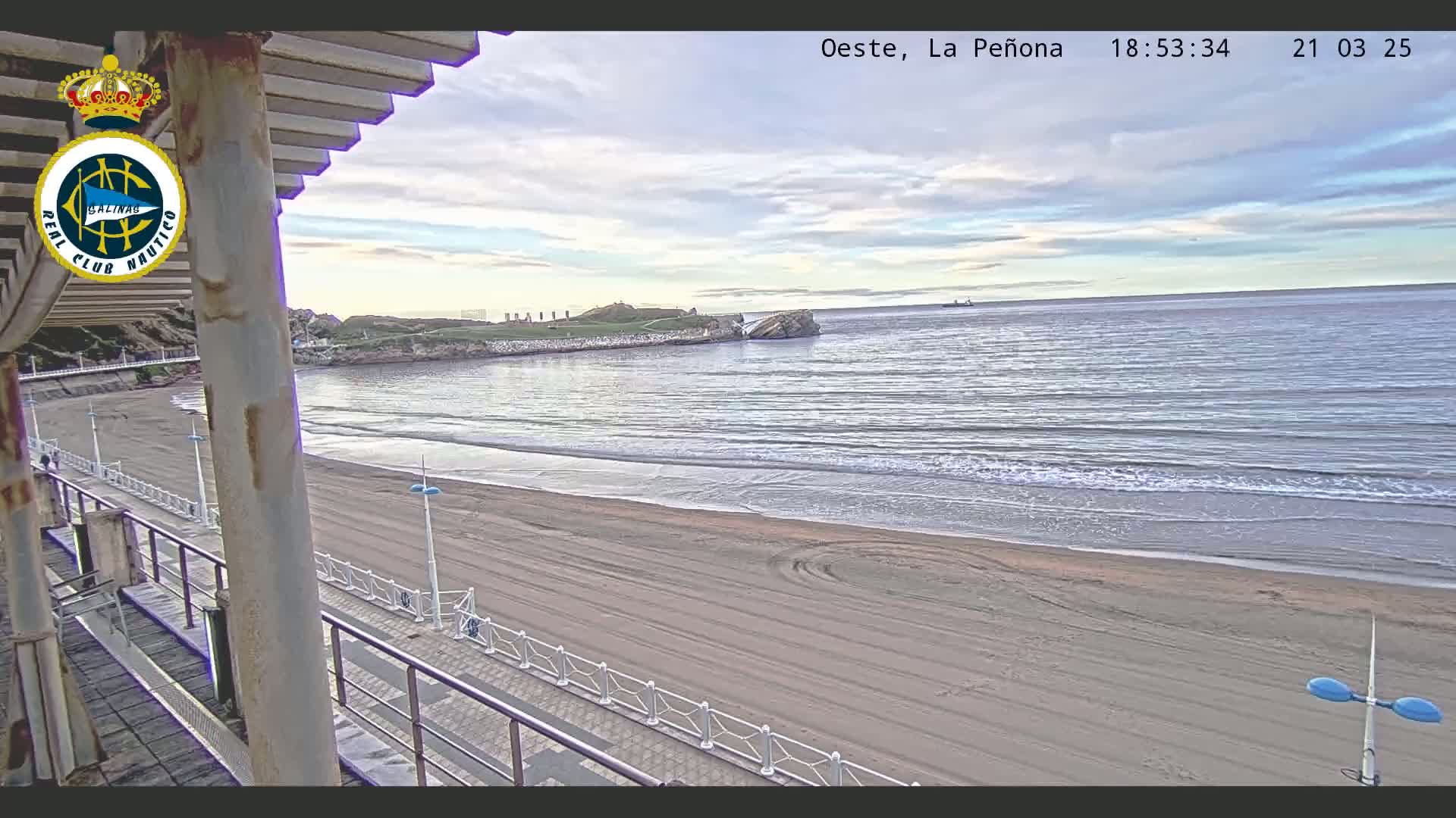 A sandy beach with calm waves under a partly cloudy sky is seen from a seaside structure.