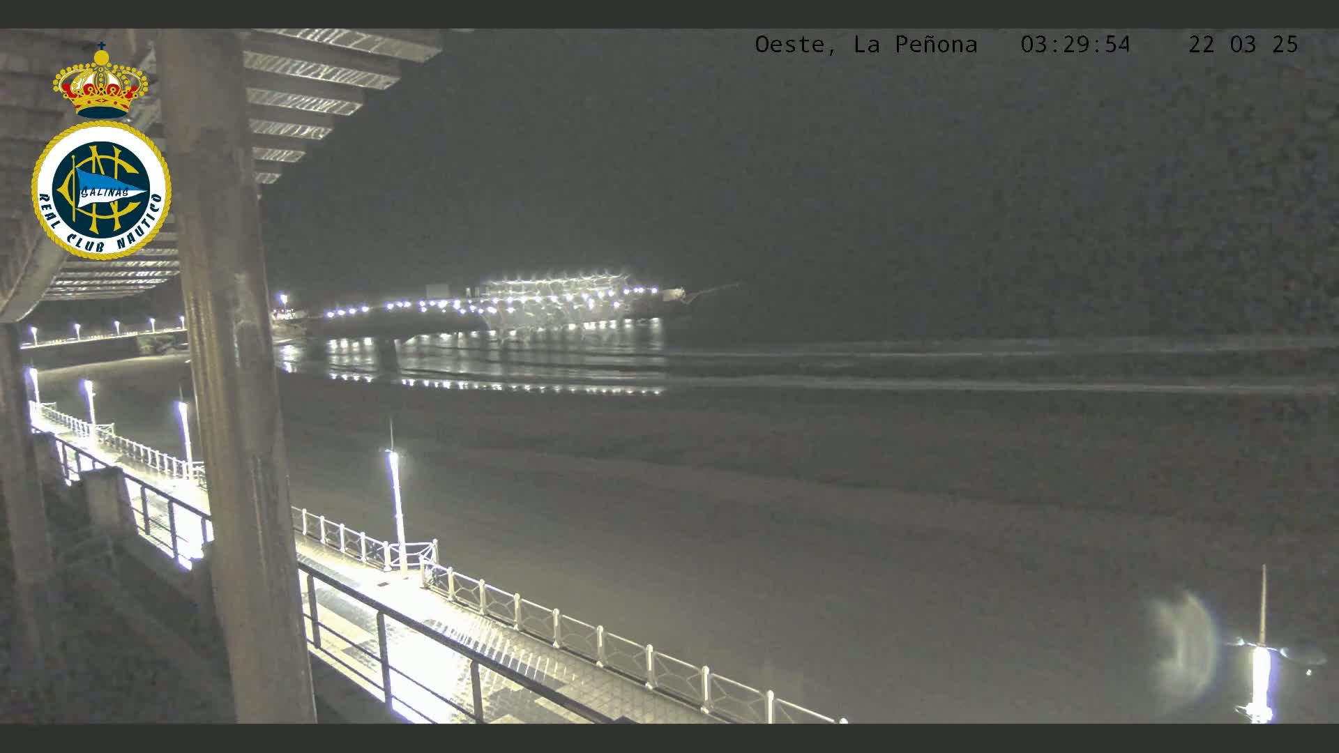A nighttime view from a pier shows a dark beach and calm ocean waves under a clear, dark sky.