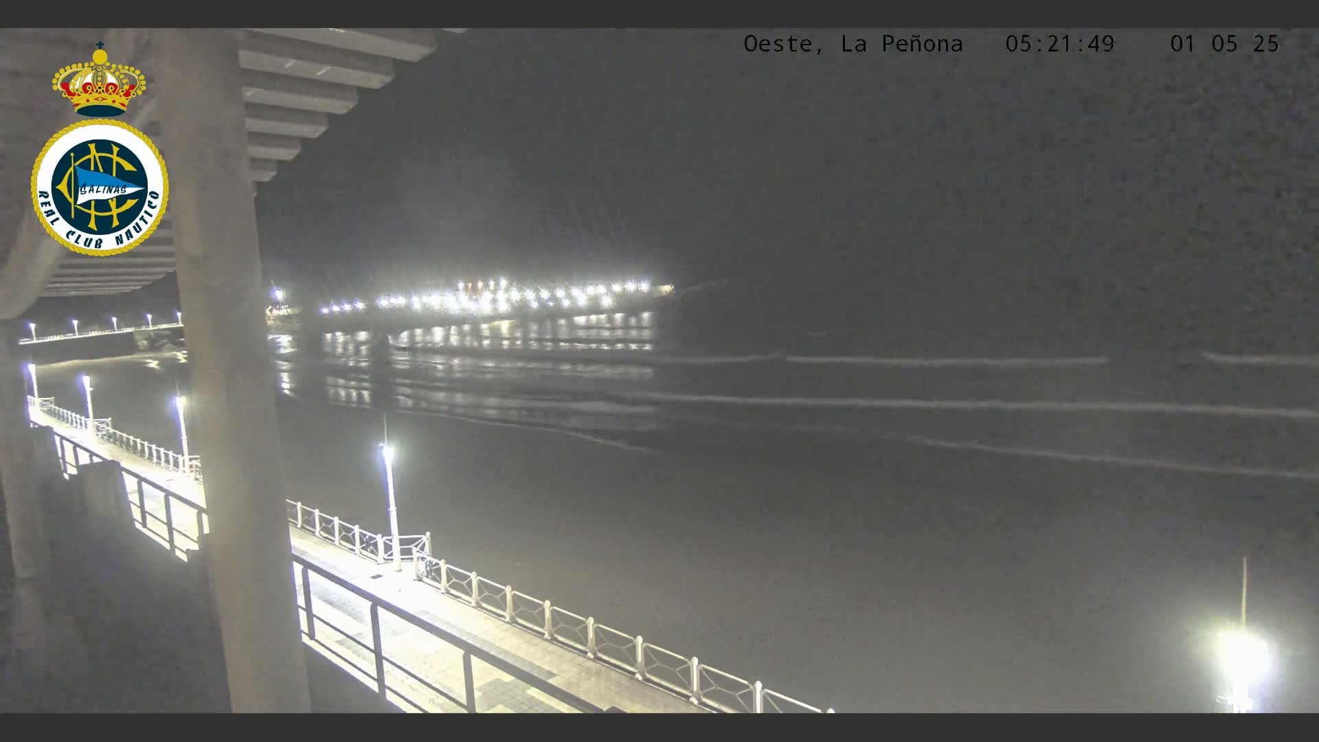 A nighttime view of a calm ocean with gentle waves lapping at a shoreline illuminated by lights from a pier and boardwalk.