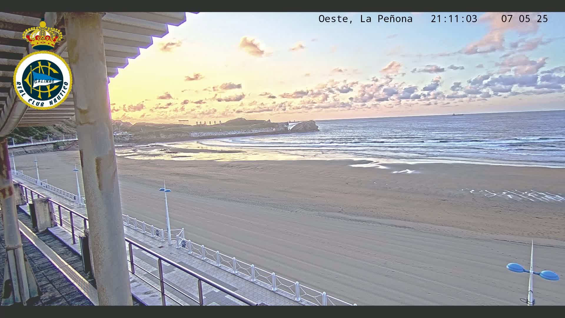 A sandy beach stretches towards a calm ocean under a sunrise sky with a few clouds.
