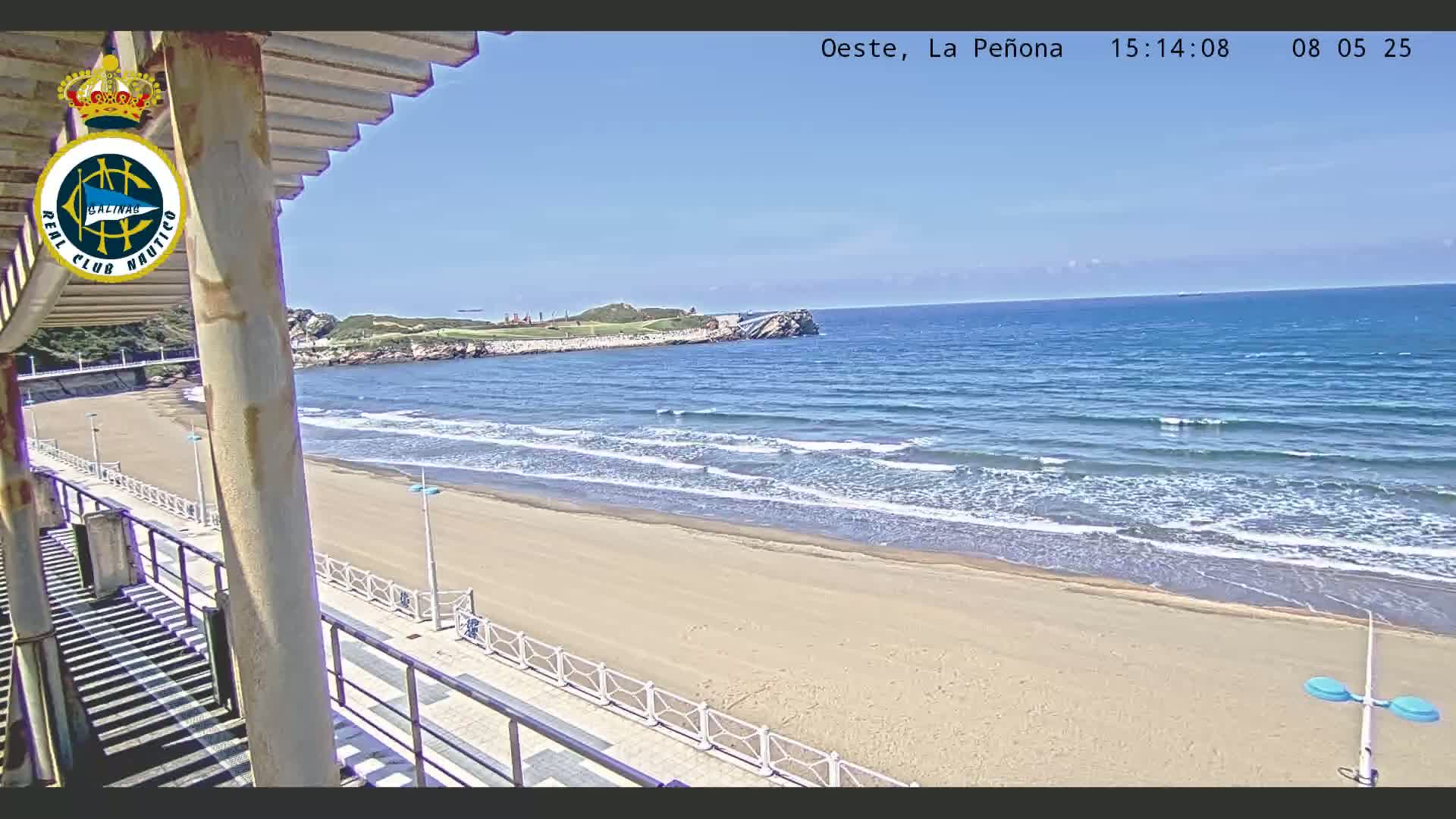 A sandy beach with gentle waves under a clear blue sky is viewed from a seaside structure.