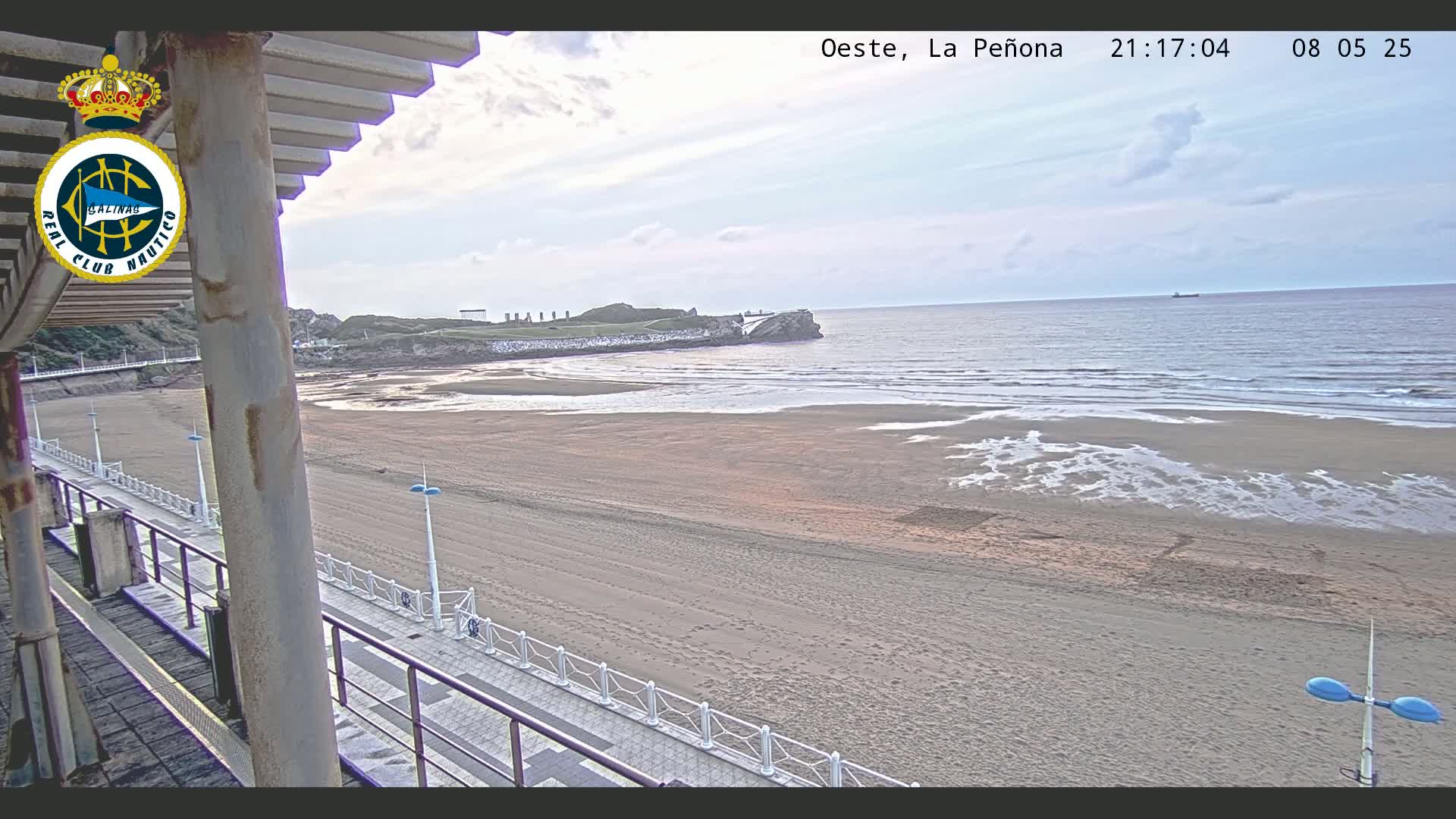 A mostly empty sandy beach stretches to a calm ocean under a partly cloudy sky.