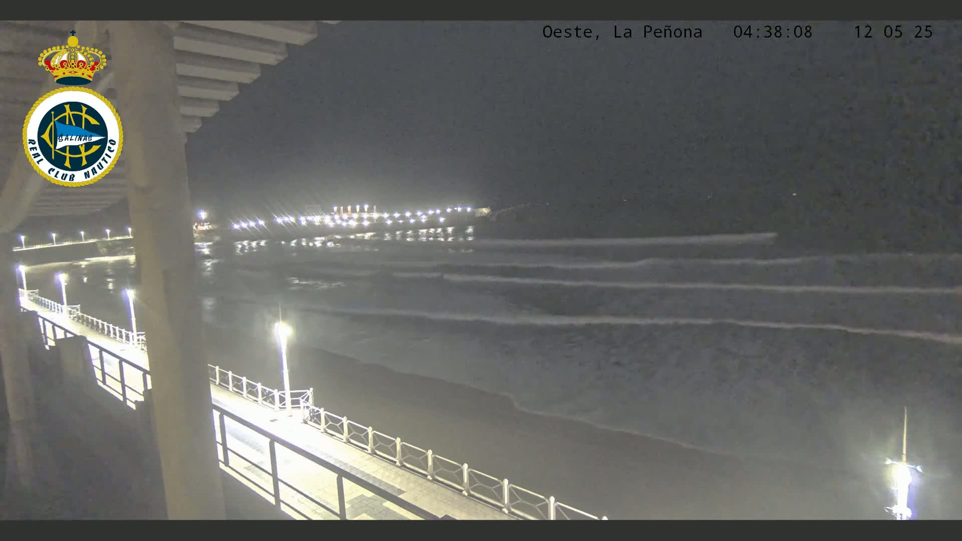 A nighttime view of a beach with gentle waves rolling onto the shore, lit by streetlights along a walkway.
