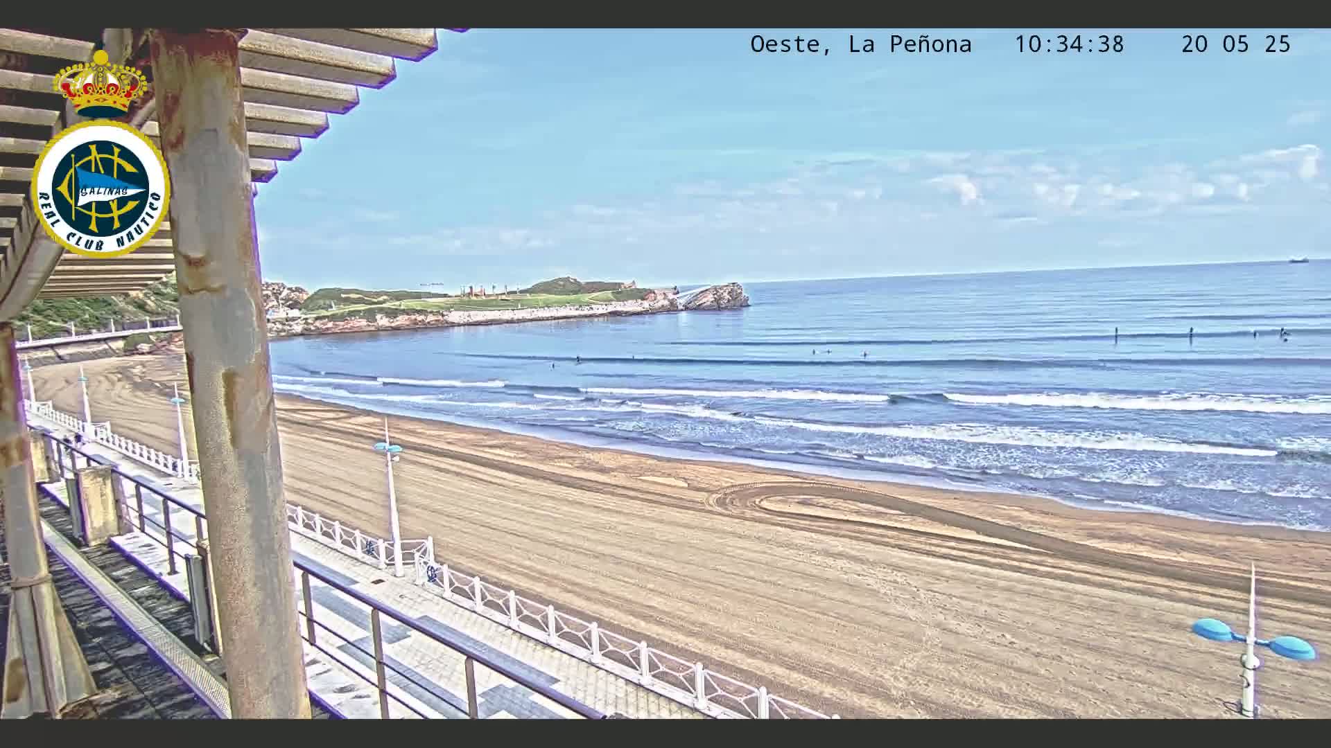 A sandy beach with gentle waves under a mostly clear sky is viewed from a seaside structure.