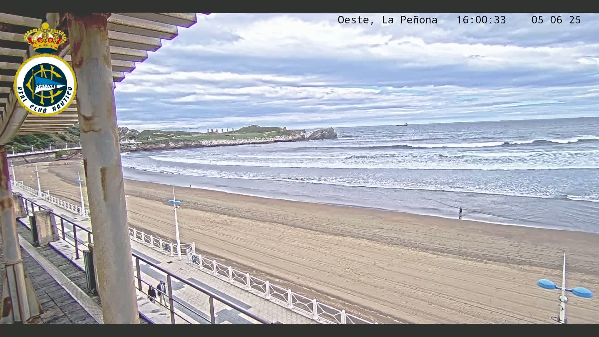 A sandy beach stretches out to a moderately wavy ocean under a partly cloudy sky.