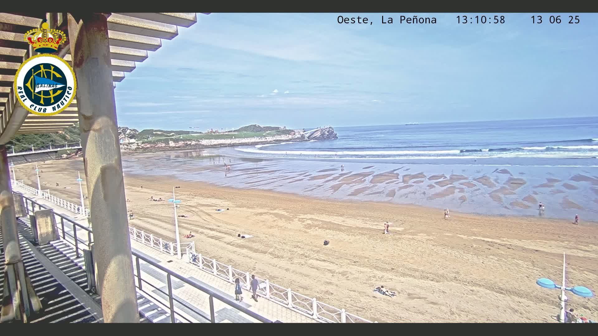 A sandy beach with a few people on it, under a partly cloudy sky, is viewed from an elevated position near a boardwalk.