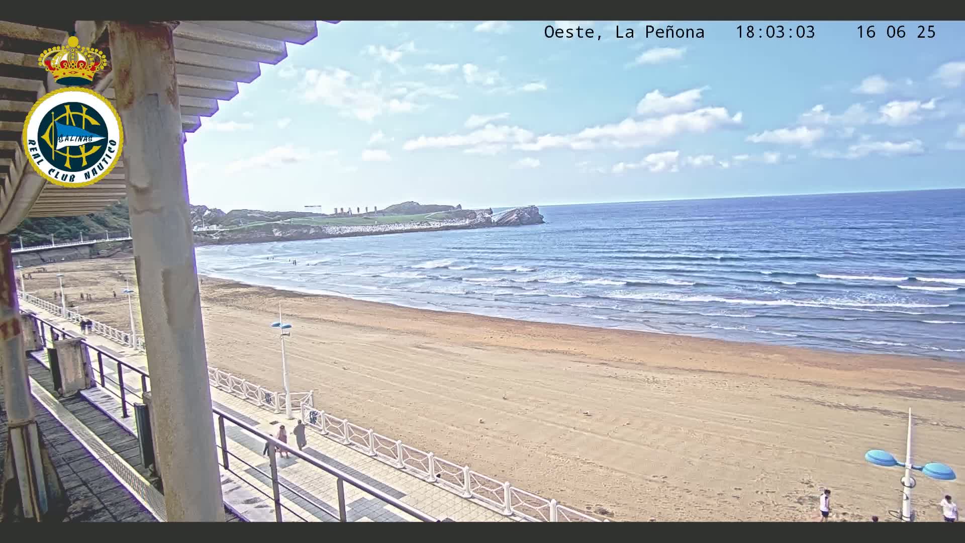 A sandy beach stretches out to a calm ocean under a partly cloudy sky, viewed from an elevated position on a boardwalk.