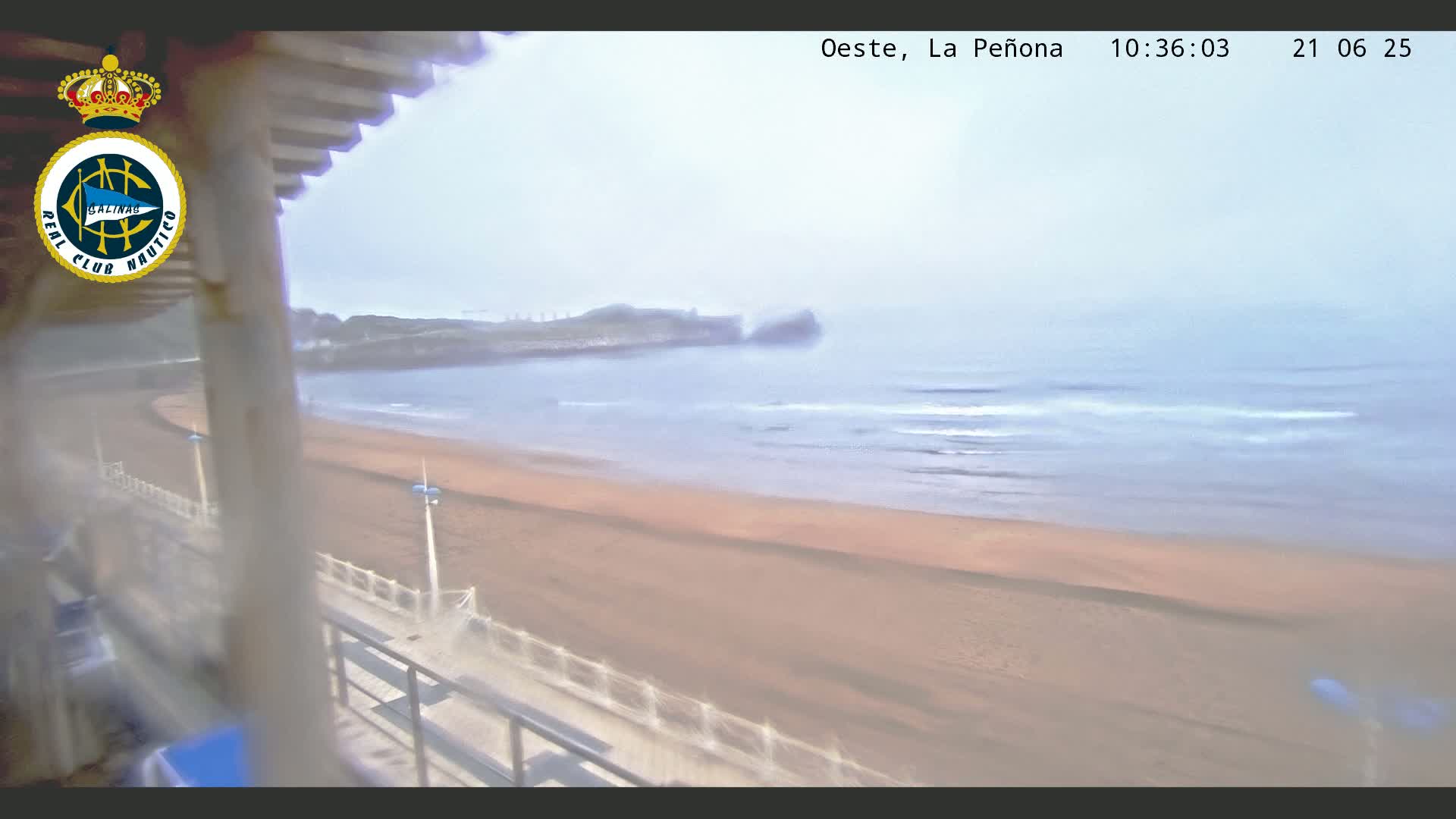 A hazy view from a balcony shows a sandy beach and calm ocean with a distant rocky outcrop.