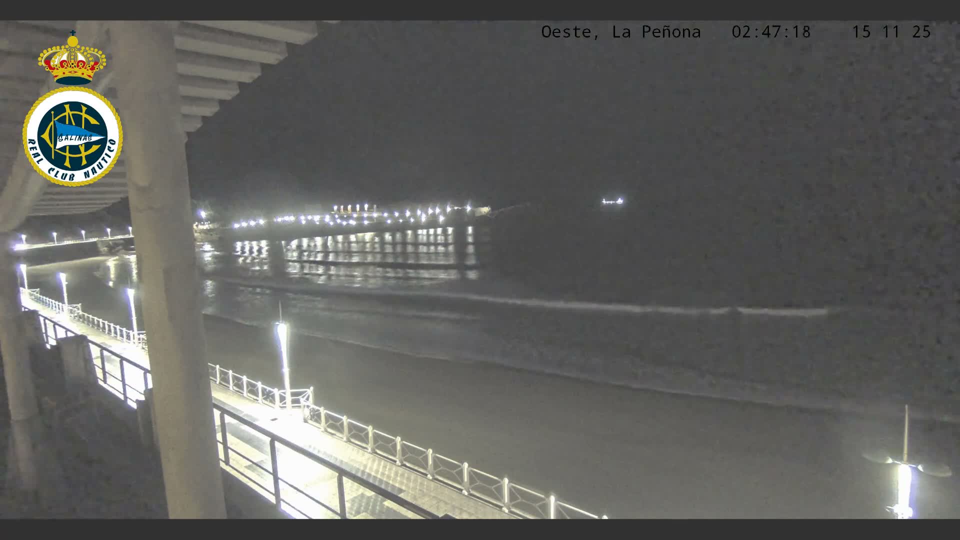 A series of brightly illuminated piers and boardwalks line a dark beach with gentle waves under a clear night sky.