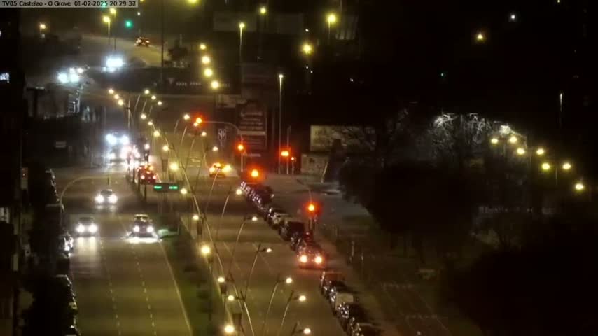 A nighttime view of a roadway intersection with several cars driving on a multi-lane road, under streetlights.