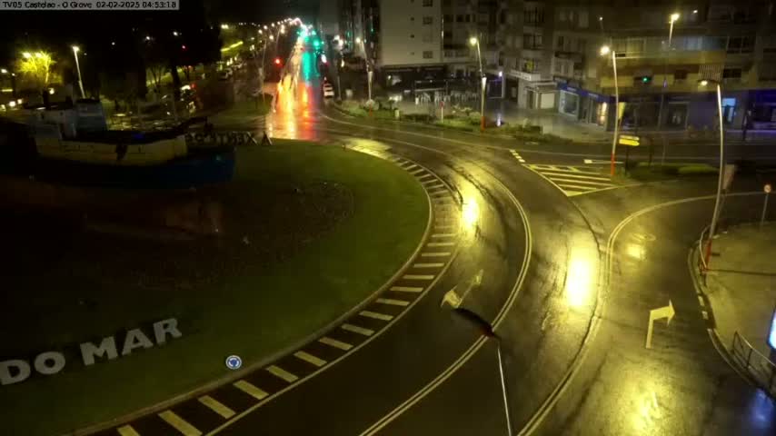 A wet roundabout at night, near a model boat, with a few vehicles visible on the roads.