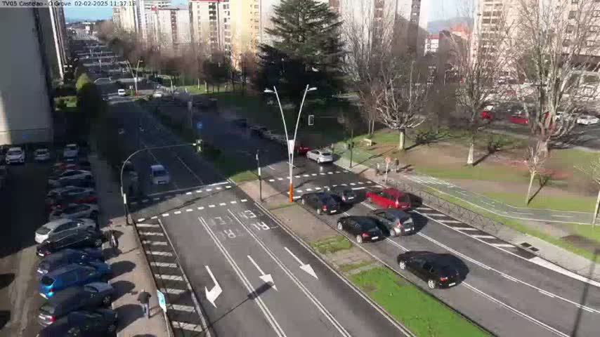 A sunny day reveals a city street scene with several cars parked along the side and others driving on the road, intersected by a crosswalk and a pedestrian path.