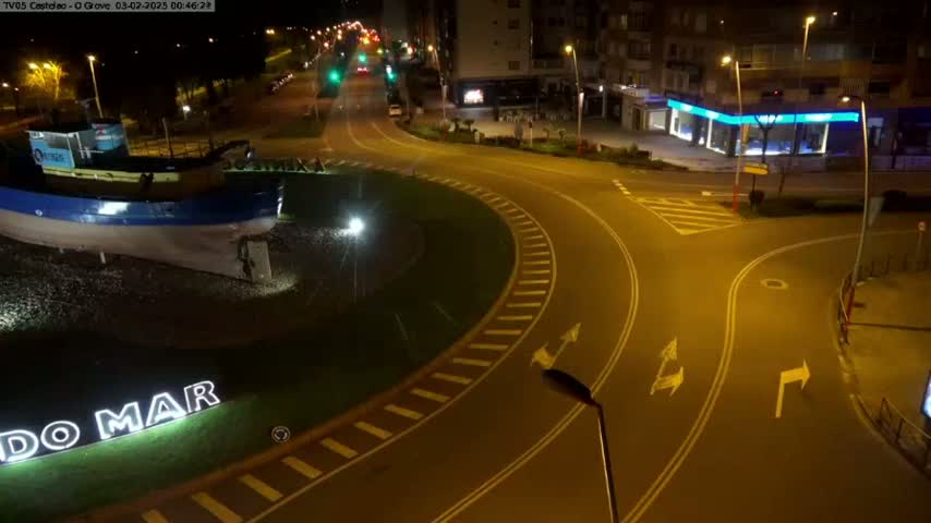 A nighttime aerial view shows a roundabout with a large boat statue in the center, surrounded by roads and buildings under well-lit conditions.
