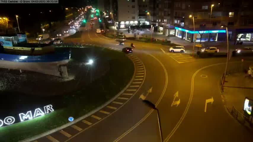 A nighttime, overhead view of a roundabout with several cars and a large boat statue at its center.