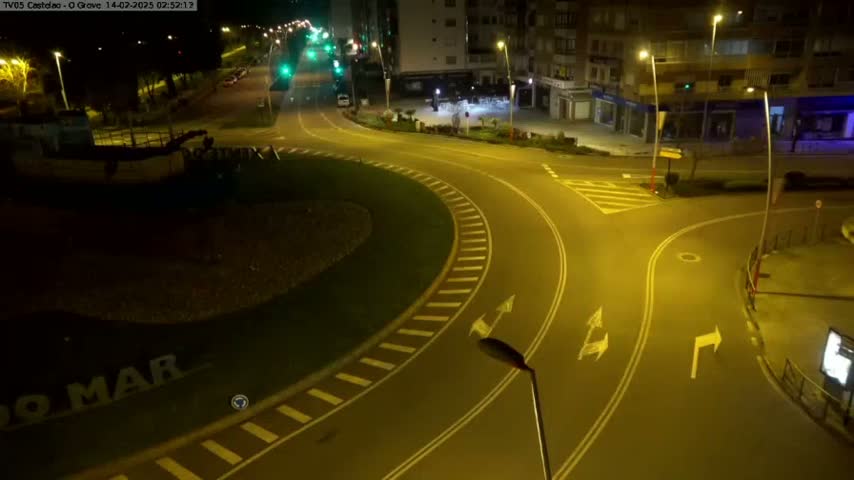 A nighttime aerial view shows a mostly empty roundabout and intersecting roads, illuminated by streetlights.