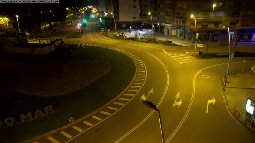 A mostly empty roundabout and intersecting roads are illuminated at night by streetlights.