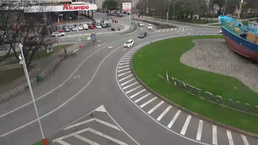 A roundabout with several cars, a large ship sculpture in the center, and a parking lot visible in the background on an overcast day.