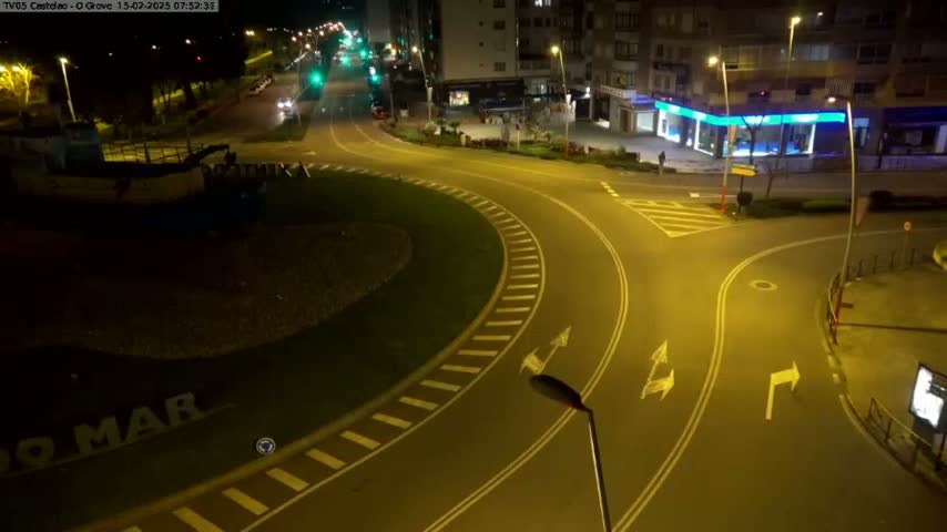 An illuminated roundabout at night, with a few cars visible on the surrounding roads.