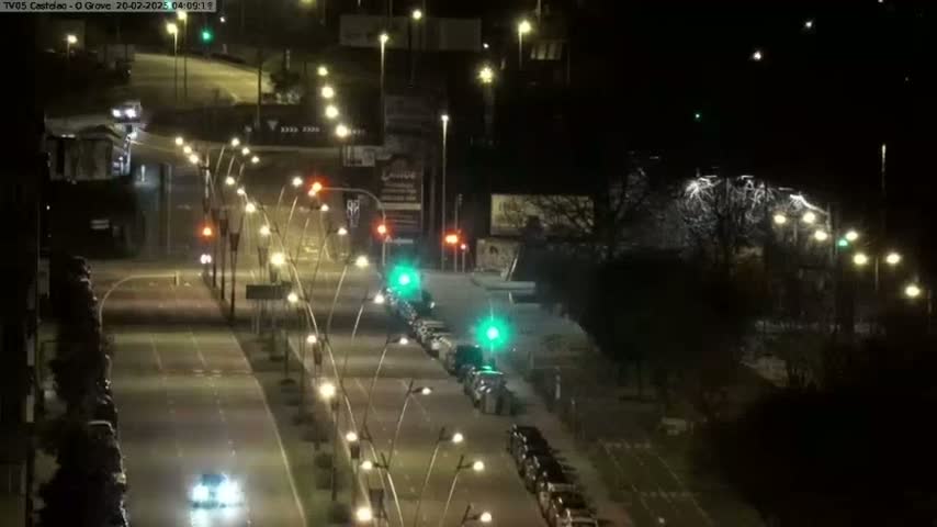 A nighttime, snow-covered road scene shows cars parked and driving along a street lined with streetlights.