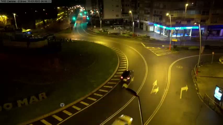 A nighttime aerial view of a roundabout and intersecting roads, illuminated by streetlights.