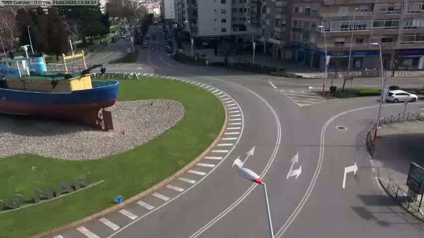 A model of a ship sits in a grassy roundabout in the center of a paved roadway on a sunny day.