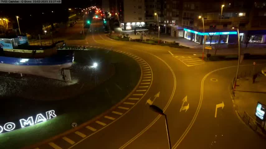 A mostly empty roundabout at night, illuminated by streetlights, features a large model boat at its center.