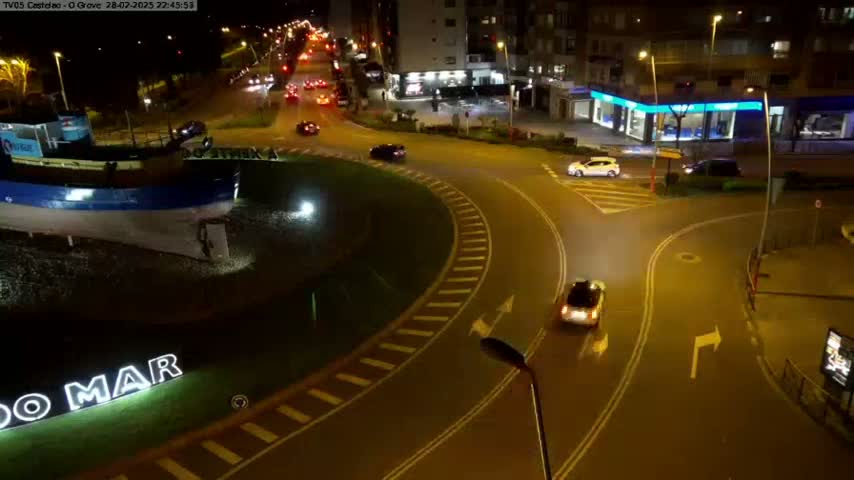 A nighttime aerial view shows a roundabout with several cars, a large model boat next to a sign that says "O MAR", and buildings in the background.