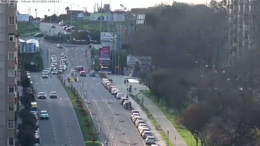 A long road with moderate traffic flows through a city under a partly cloudy sky.