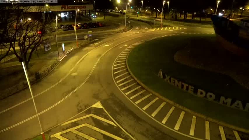 An aerial nighttime view of a roundabout with a grassy center, illuminated by streetlights.