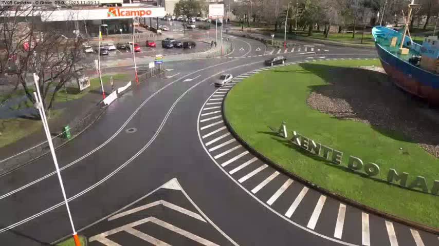 A wet roundabout with a few cars, a large ship sculpture in the center, and a parking lot in the background.