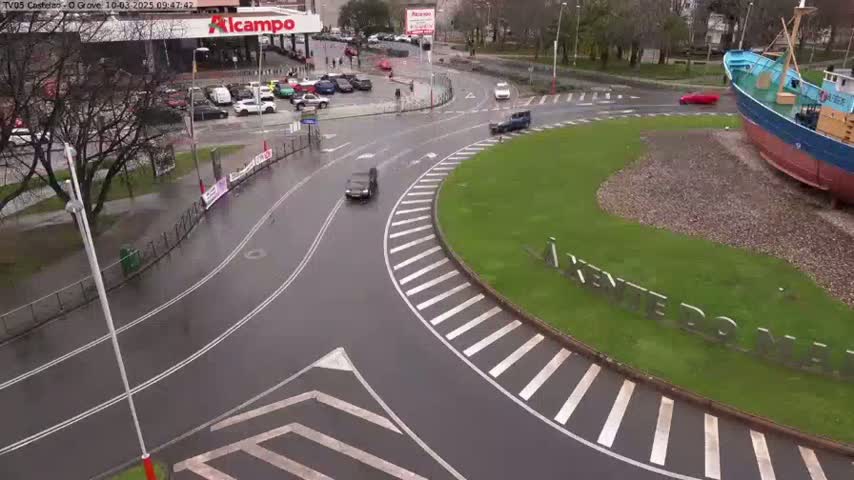A wet roundabout with several cars and a large fishing boat visible in the background.