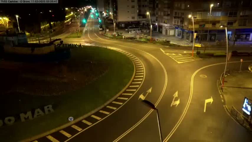 A nighttime view of a mostly empty roundabout and intersecting roads, illuminated by streetlights.