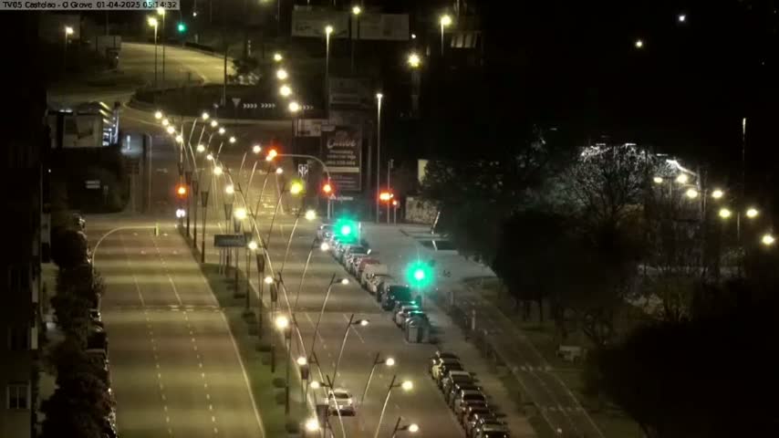 A nighttime view of a multi-lane road with cars parked along the side and streetlights illuminating the scene.