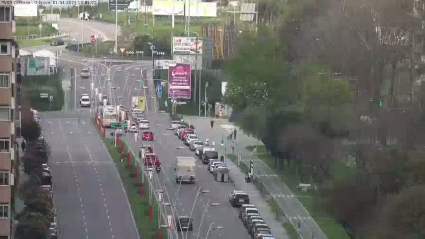 A multi-lane road with moderate traffic flows through a tree-lined area on an overcast day.