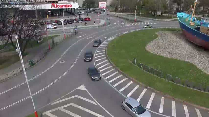 Several cars are driving around a roundabout on a sunny day, next to a large, beached fishing boat.