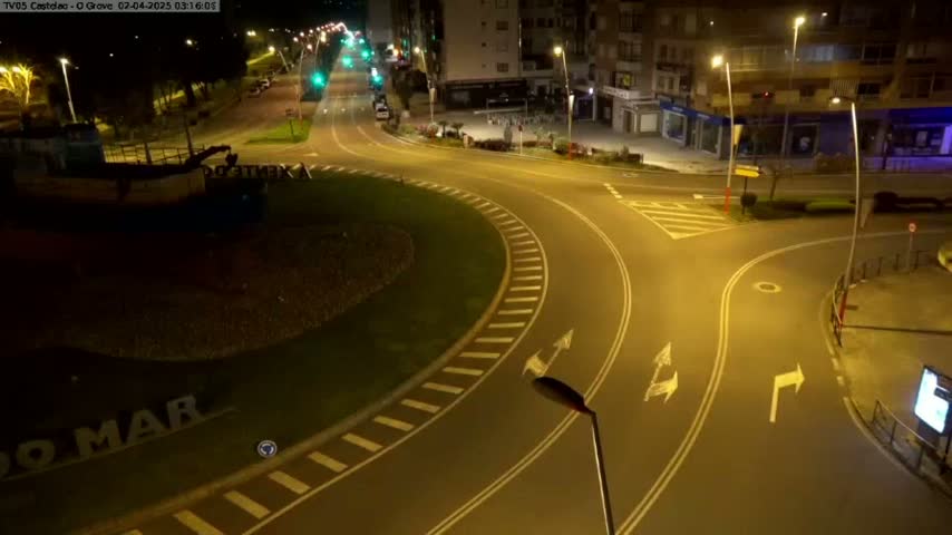 A mostly empty roundabout at night, illuminated by streetlights, with buildings visible in the background.