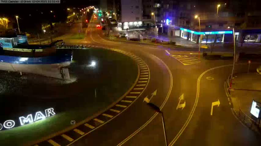 At night, a large boat sits in a roundabout next to a wet roadway with light traffic.