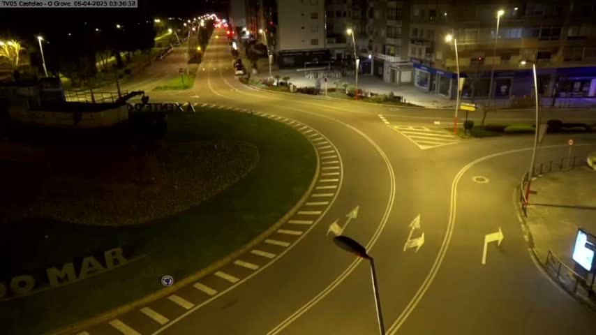 A mostly empty roundabout and intersecting roads are illuminated at night by streetlights.