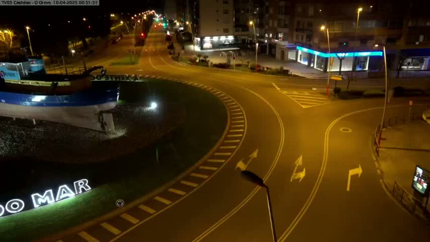 A nighttime, high-angle view shows a roundabout and intersecting roads with a boat sculpture at the center of the roundabout.
