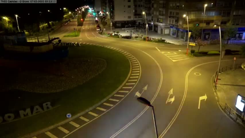 A mostly empty roundabout at night, illuminated by streetlights, with a boat visible in the lower left corner.
