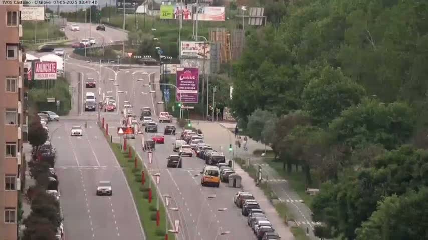 A multi-lane road with moderate traffic flows through a tree-lined area on an overcast day.