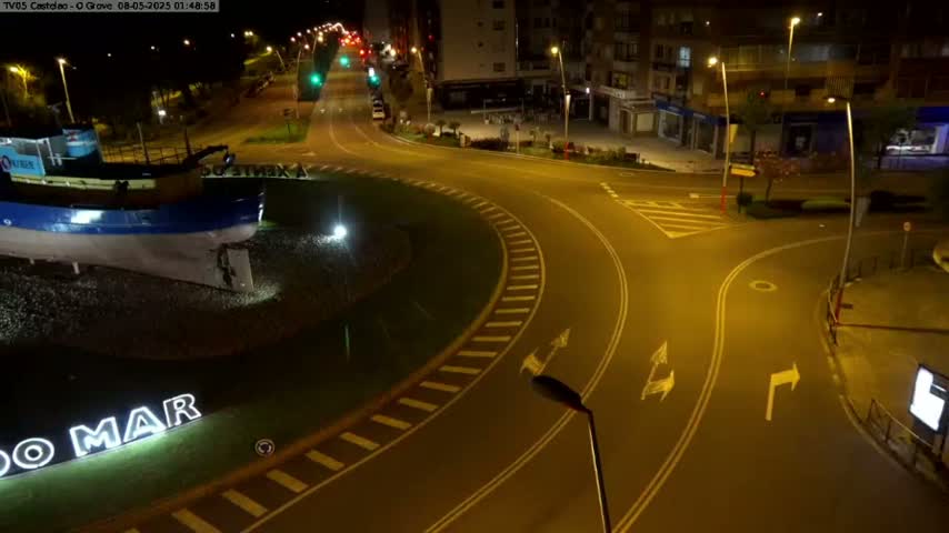 A nighttime view of a mostly empty roundabout with a boat statue at its center, surrounded by buildings and roads lit by streetlights.