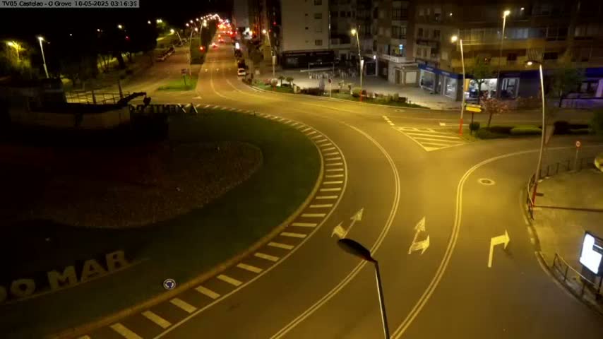 A mostly empty roundabout and intersecting roads are illuminated at night by streetlights.