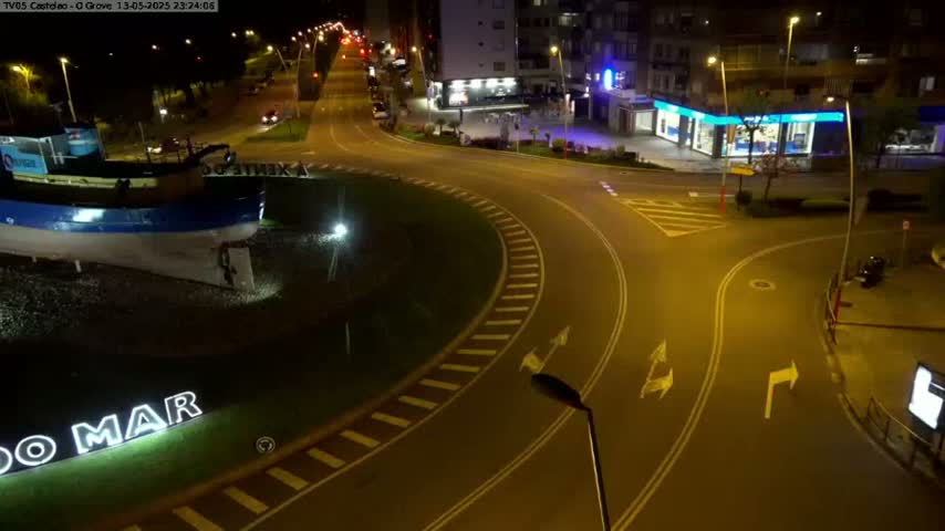 A nighttime view of a roundabout with a large boat sculpture at its center, surrounded by streets and buildings under artificial lighting.